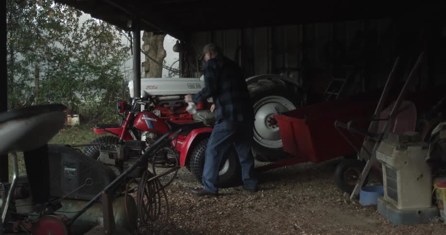 A man gets on an atv parked next to his tractor and tries to start it up