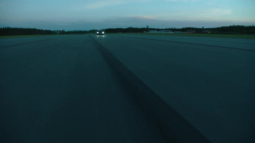 Car drives along straight road past forest and fields