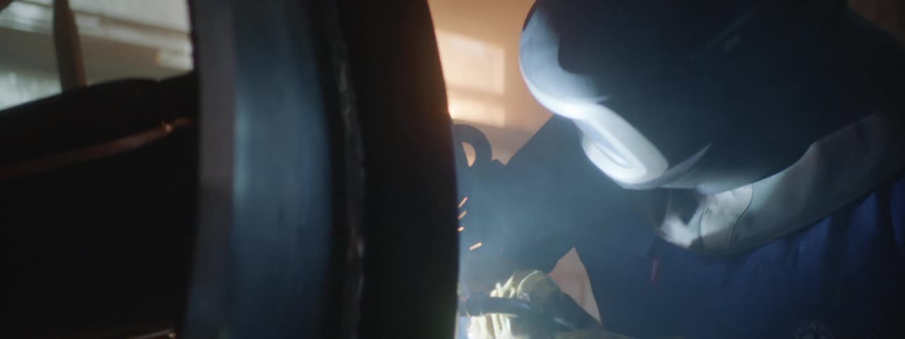 A person is kneeling in a workshop while cutting through metal with a blowtorch