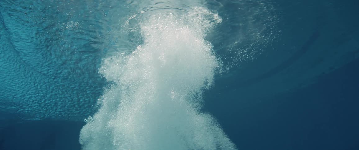 Column of bubbles form white column raising to water surface and creating concentric ripples