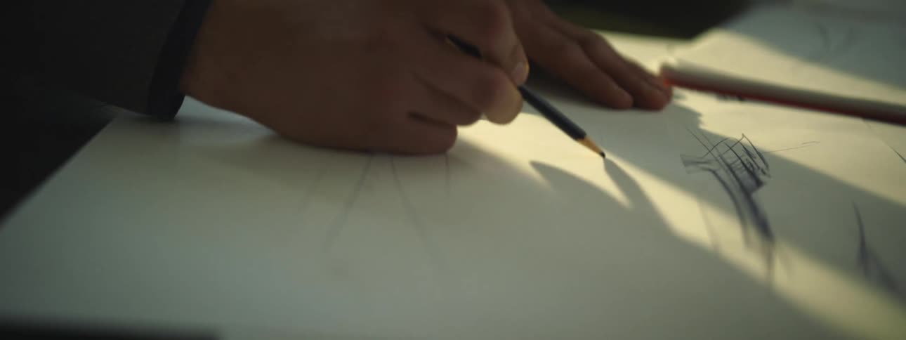 A pair of people use pencils to draw on sheets of paper on a table