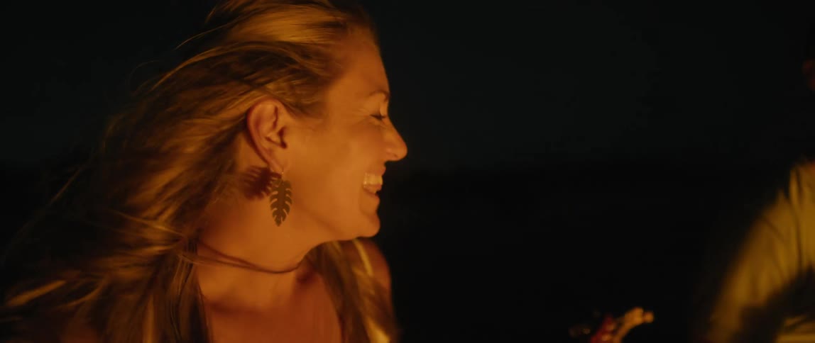 Blonde woman and male friend play guitar sitting outside at night