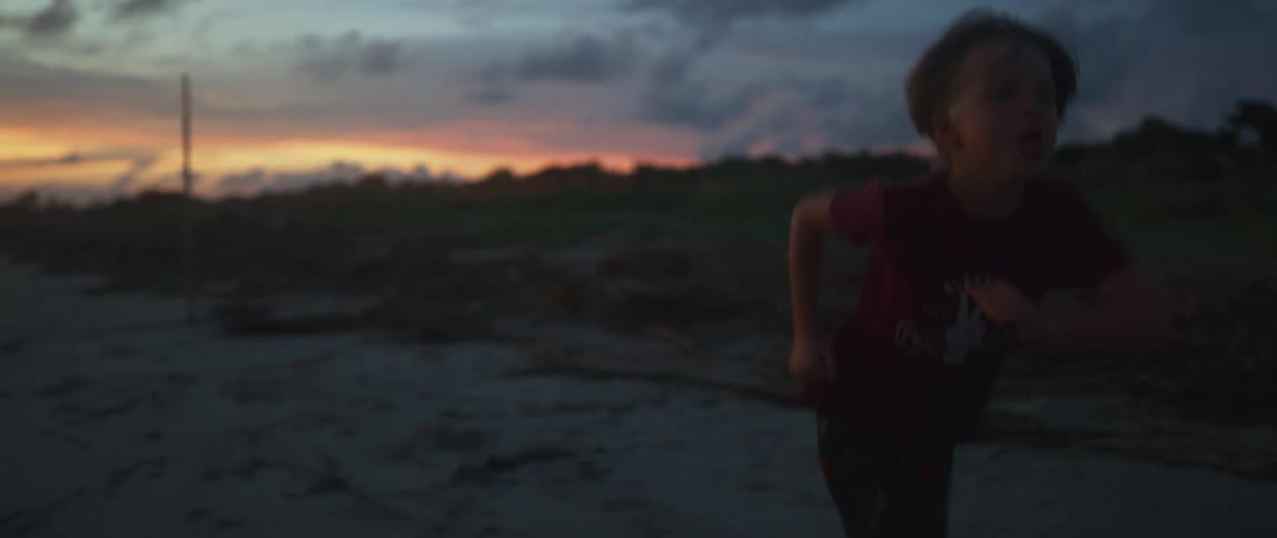 Toddler boy with red t shirt stands on the beach and plays around at dusk
