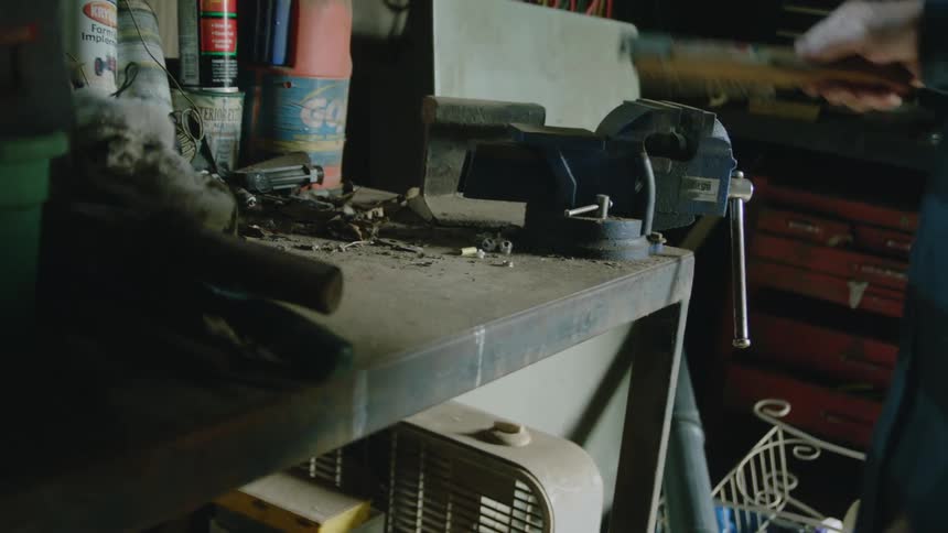 A man uses a wire brush to clean up power tools and his work bench in a tool shed