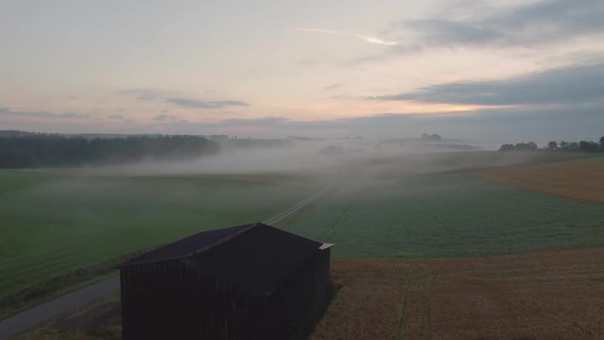A barn in the middle of a large misty field
