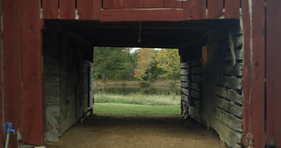 A pond and trees are visible behind a red plank barn