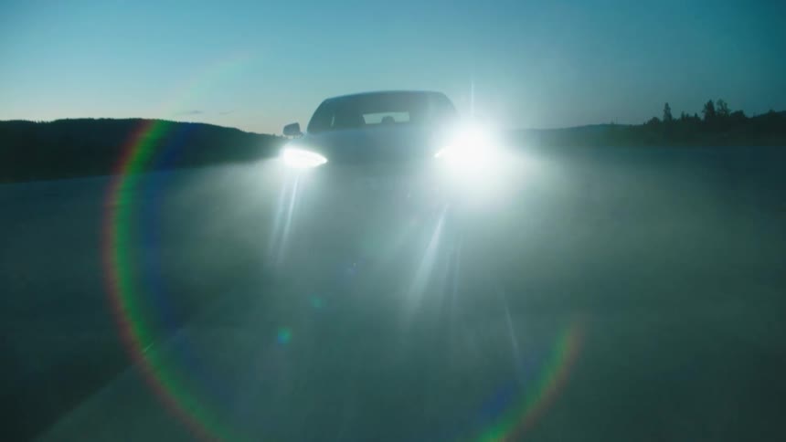 A car is traveling on a road with the headlights on as fog and rain reflect in the light