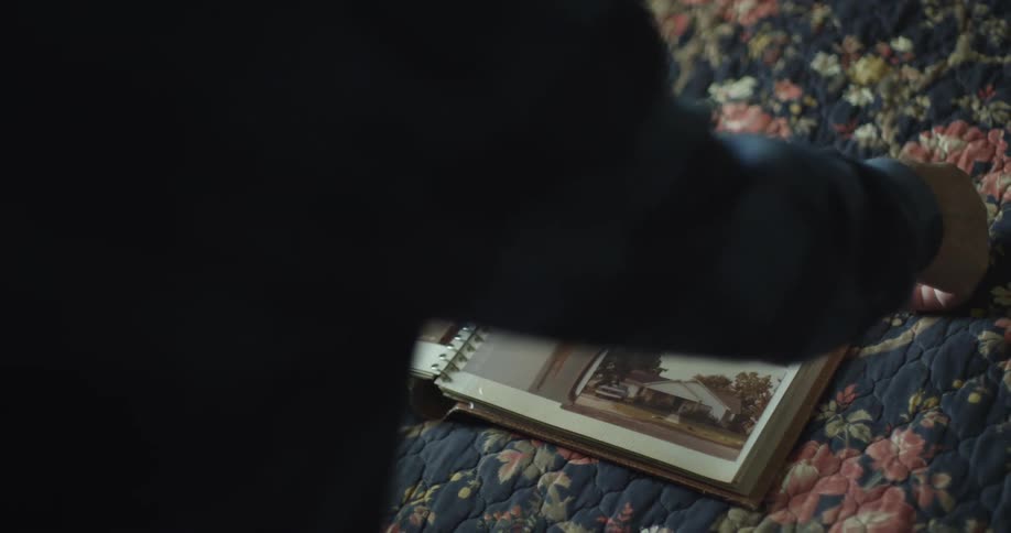 A woman thumbs through a spiral bound photo album laid out on her bed