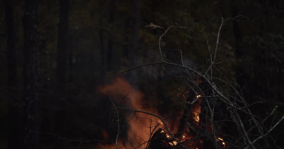 A man walks past a burning campfire