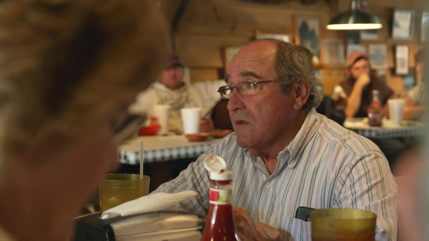A man nods his head and chats with his companions while eating in a restaurant