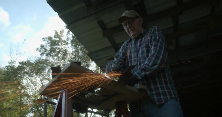 Sparks fly as a man uses a power tool on metal on his workbench