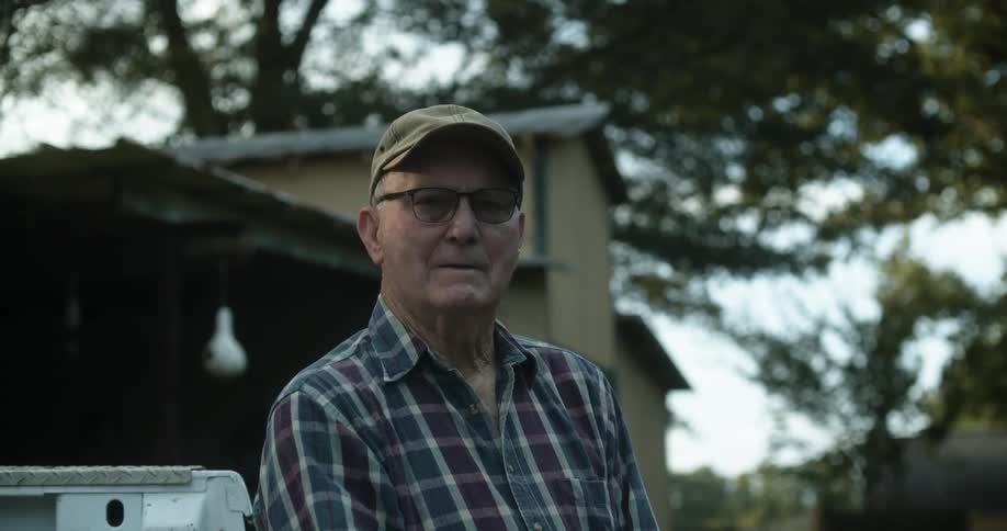Man wearing baseball cap and plaid shirt poses outside home