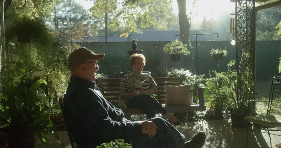 Elderly couple sit outside on chair and bench swing talking