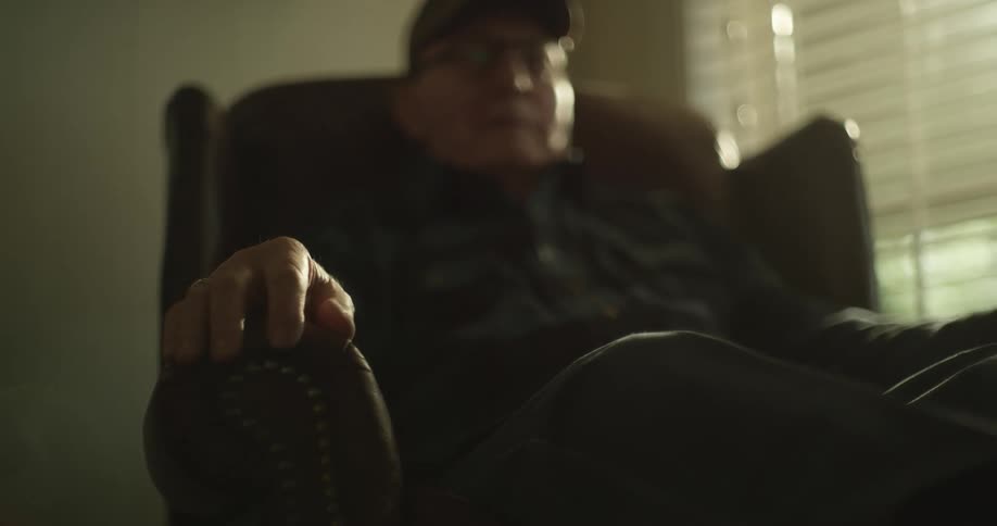 An elderly man sits in an armchair in a house during the day