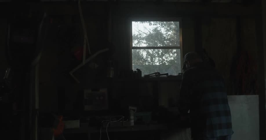 An elderly man stands in a dark room and looks at some equipment