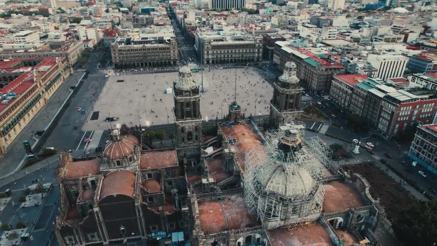 An aerial view of a large church surrounded by buildings with cars driving on streets in a city
