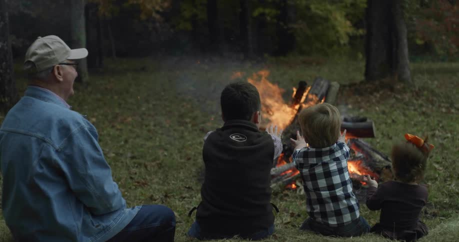 An elderly man watches as his grandchildren hold their hands up to feel the heat from a bonfire