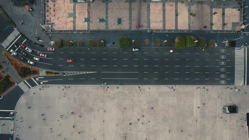Aerial view of many people walking on a large concrete area near a road where cars are traveling by old buildings