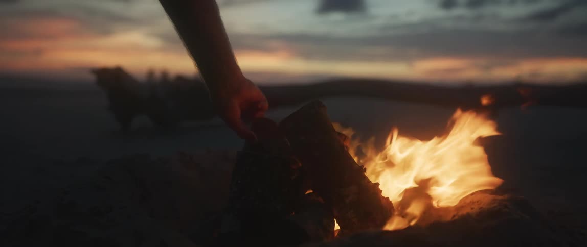 Person places a log on campfire at dusk
