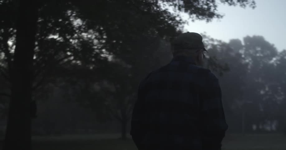A man puts his hands in his pant pockets while walking along a tree line in a park