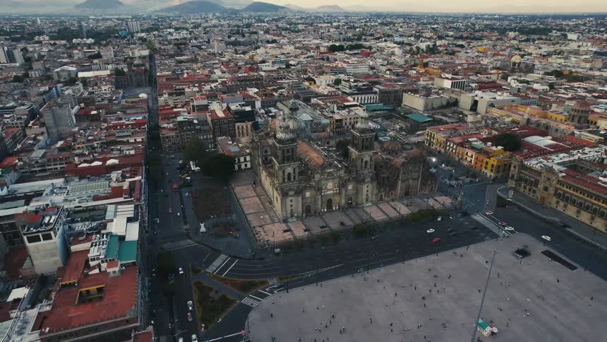 Traffic flows along streets near cathedral in city stretching toward the mountains