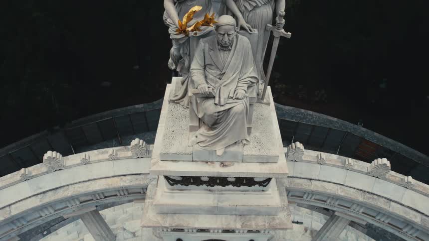 A statue of three people is in front of the trees