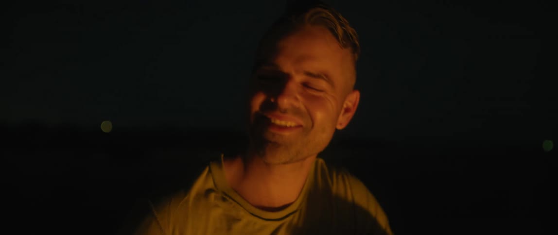 A man is outside at night smiling and singing as light shines on his face