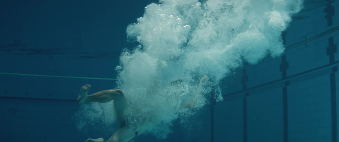 A man jumps in to a pool of water and bubbles rise to the surface