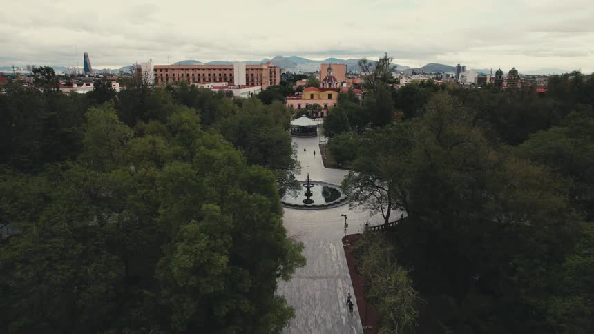 People walk on the paved path of the alameda central park near a fountain with the benito jurez hemicycle monument at the entrance