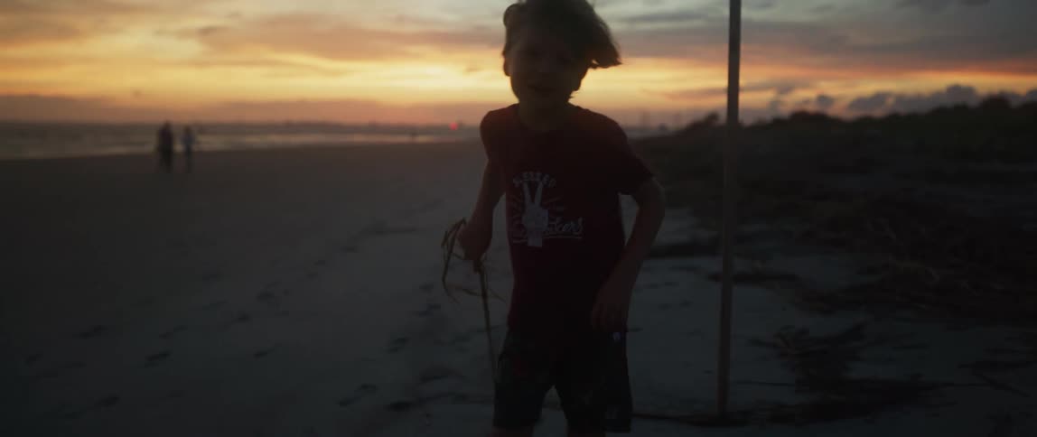 A boy plays with a stick on a beach at sunset