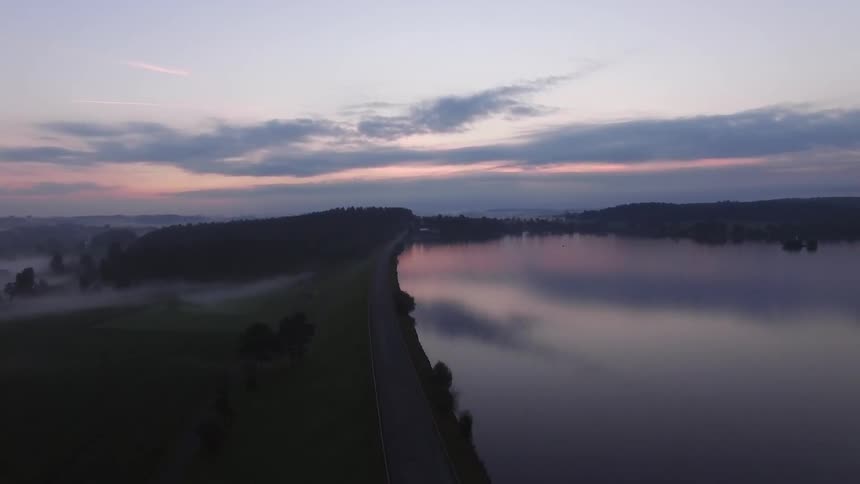 The sun is setting past this cliff near a lake