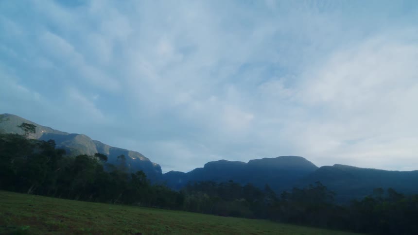 Clouds on the blue sky at morning over a grass field near the mountains