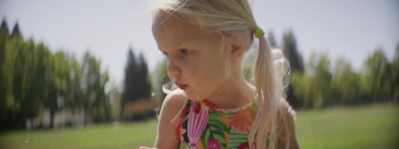 Young girl wearing a dress blows a dandelion from her hand on a field