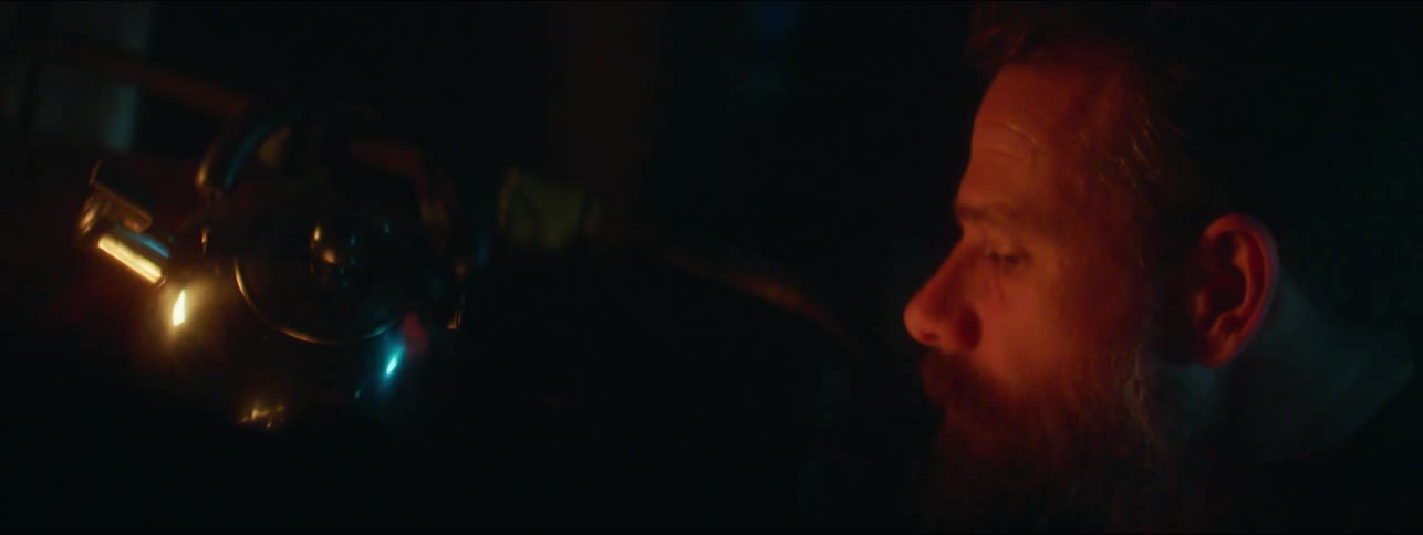 Man with beard sits next to fire in the cabin at night