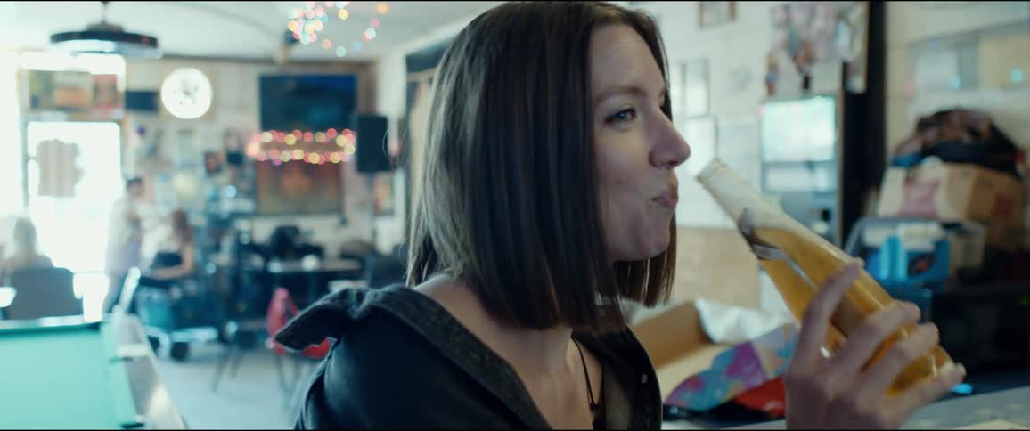 A woman in a bar takes a drink of a beer and smiles