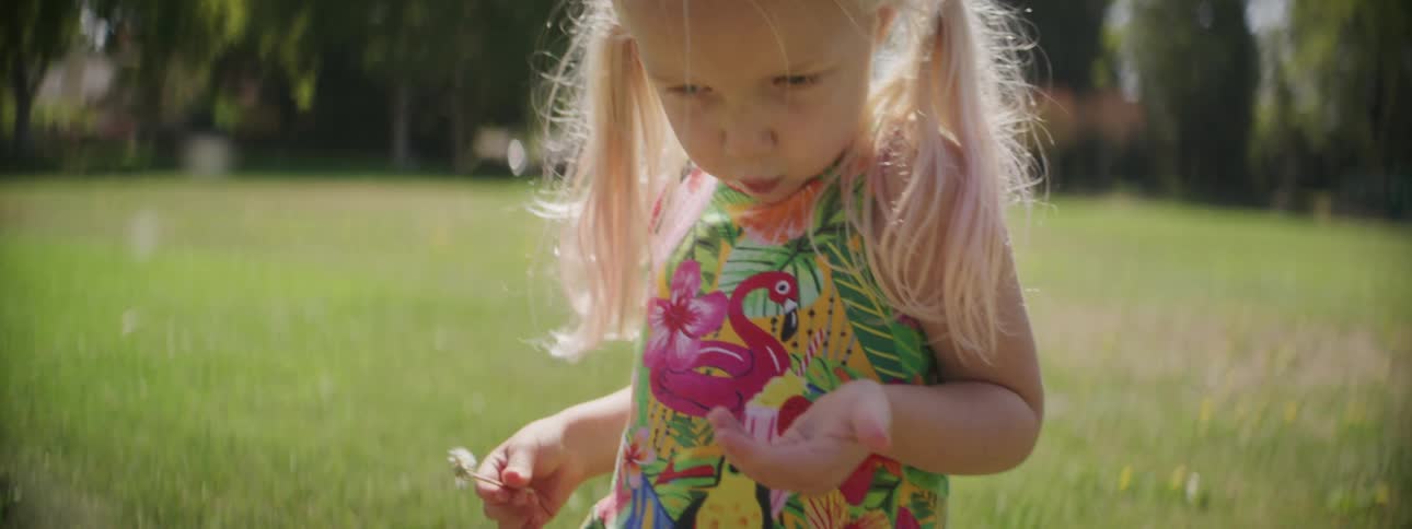 Blonde girl blowing a dandelion from her hand in the backyard