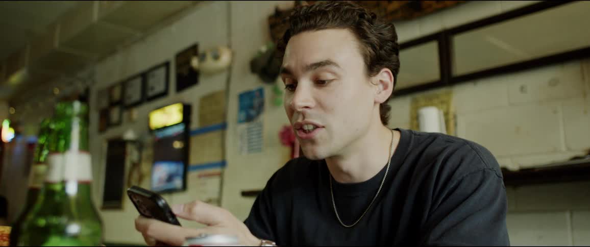 Young man sitting at a table in a restaurant talking to a friend while checking his phone