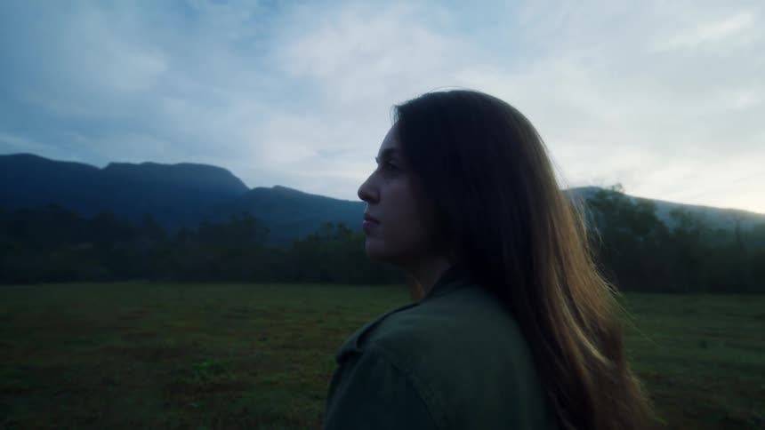 A woman stands on the field looking at the mountains