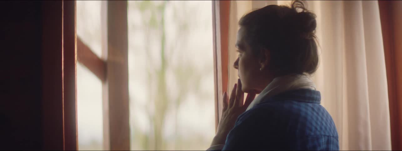 A worried woman rubs her face by the window