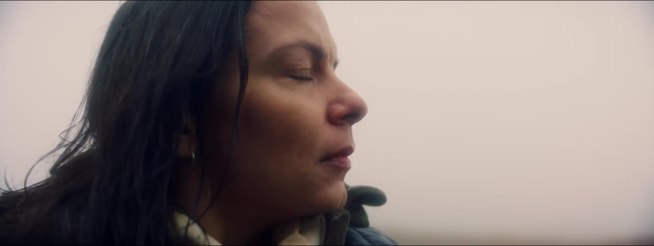 Woman stands outdoors looking then closes her eyes and breathes deep