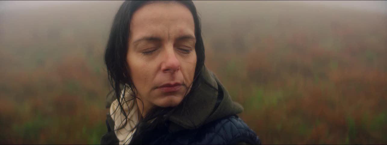 Woman closes her eyes outdoors on a cloudy day with fog