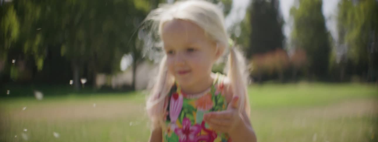 A child is blowing a dandelion in the yard