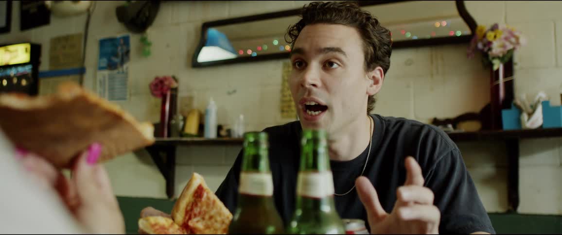 A man is sitting at a table holding a pizza at a restaurant and talking to a woman