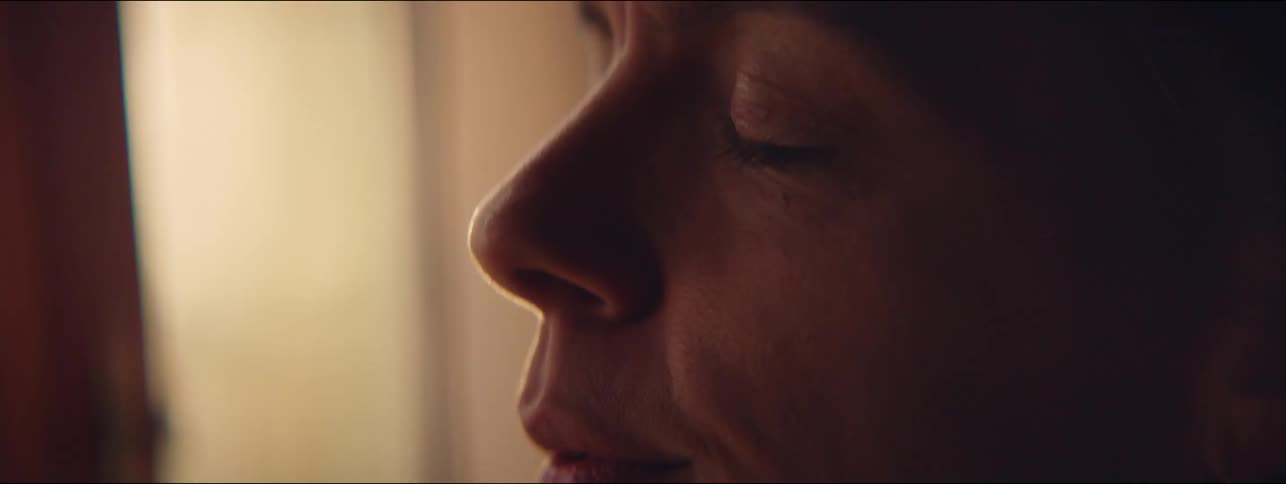 A woman closes his eyes and takes a deep breath while standing near a window