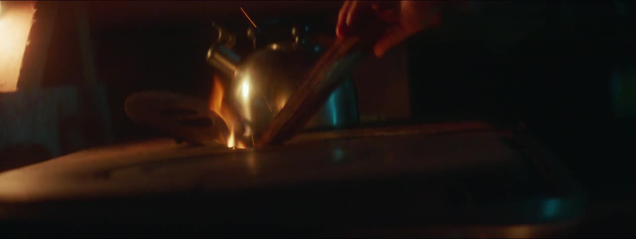 A man at home uses a piece of wood to adjust a flame on a wood burning stove