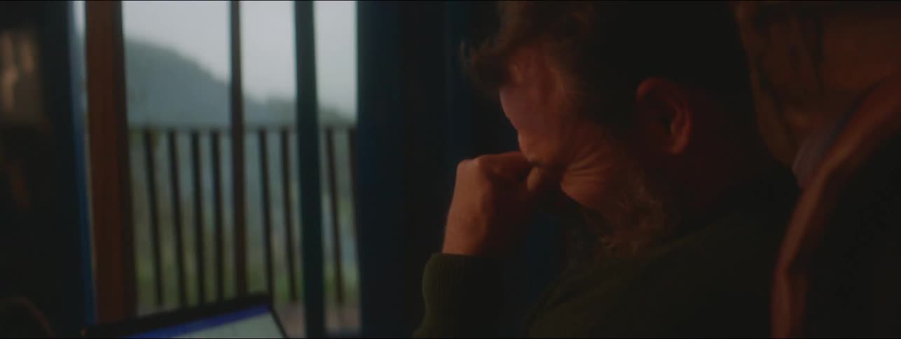 A tired man is working on a laptop in a cabin located on a forested mountain in the evening