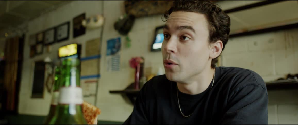 Young man sitting at a table on a restaurant eating pizza while talking to someone