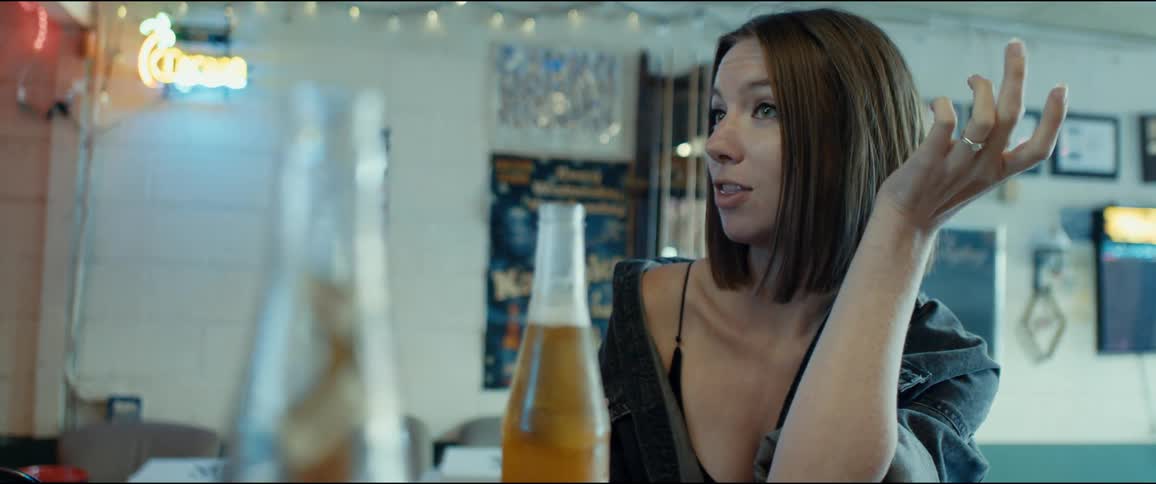Woman sits at bar with beer bottles talking