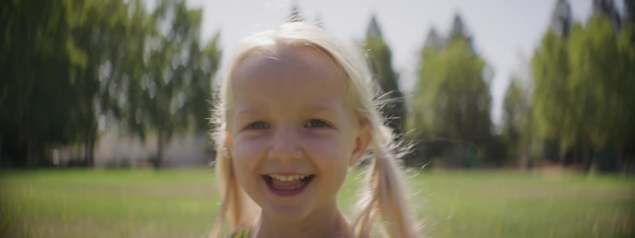 A young girl walks across a grassy field smiling as she carries a dandelion