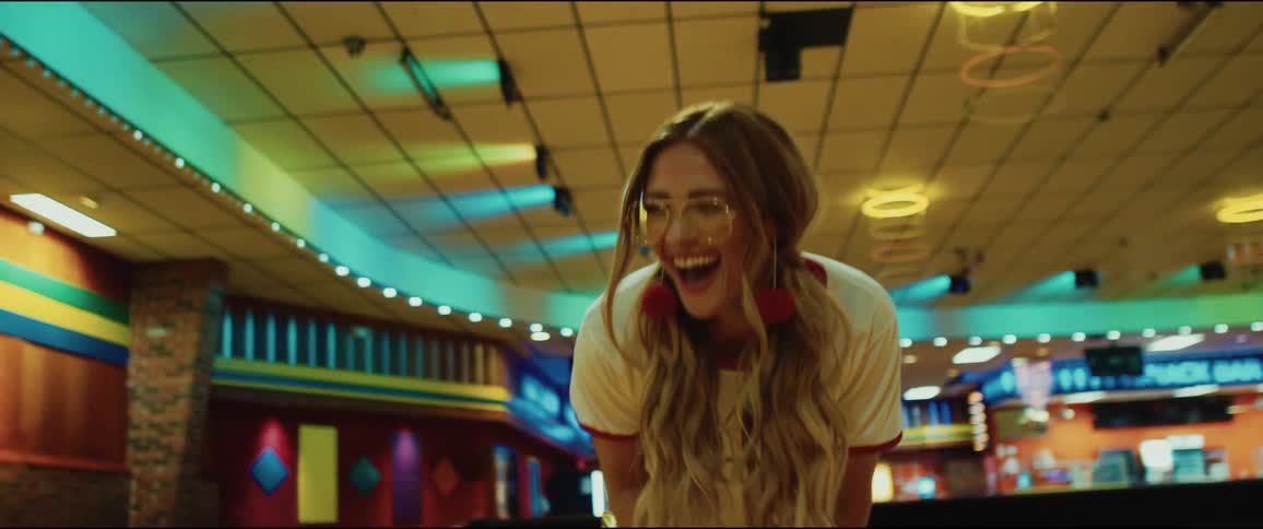 A teenage girl on roller skates in a roller rink bends down and laughs